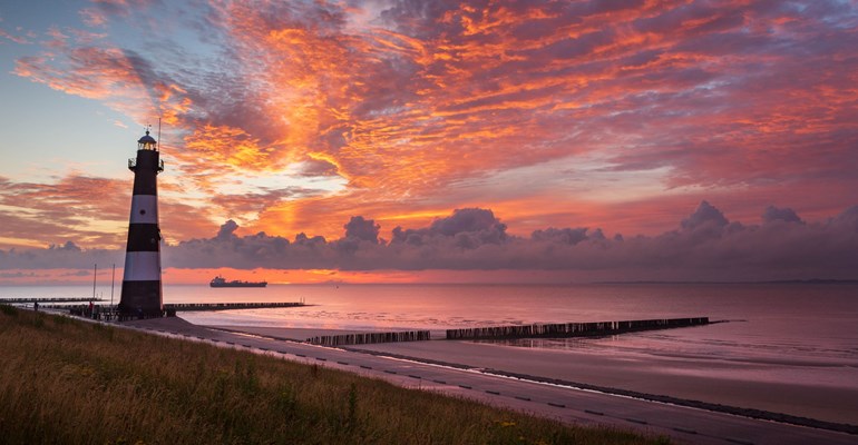 Zonsondergang in natuurgebied met op de achtergrond woningen in Zeeland.
