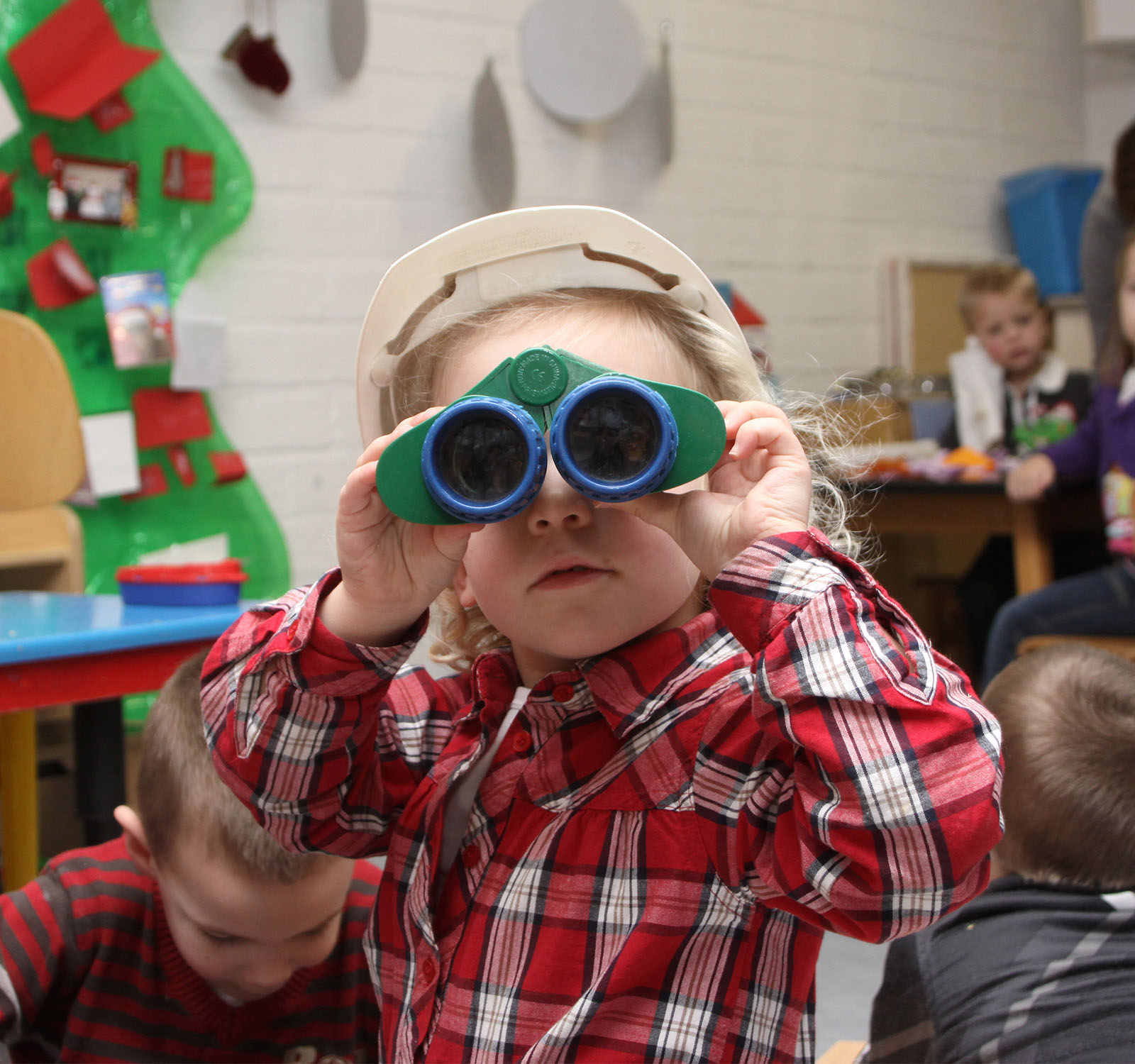 Kind kijkt op de kinderopvang door verrekijker naar de camera.