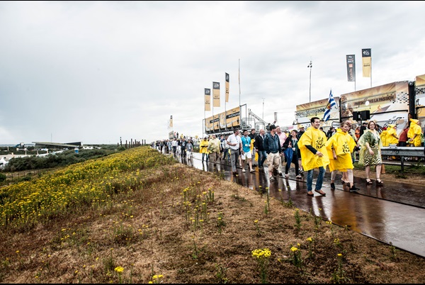 Toeschouwers van de Tour de France lopen op de Oosterscheldekering in een gele poncho in de regen