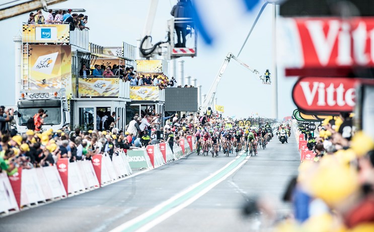 Wielrenners gaan finishen op de Oosterscheldekering tijdens de Tour de France, honderden mensen staan de wielrenners aan te moedigen