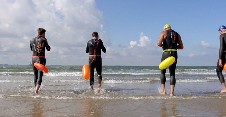 Vier personen met duikpak aan gaan zwemmen aan de zee in Vlissingen